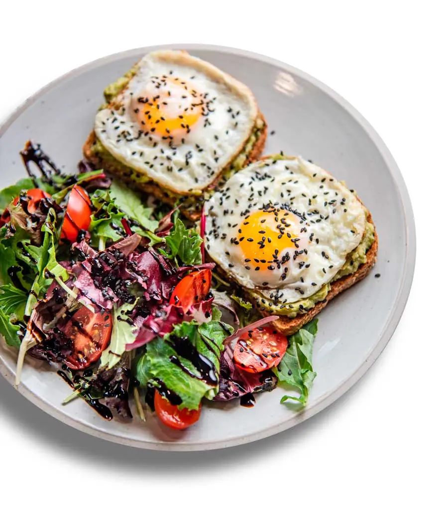 Avocado toast topped with eggs, served with a fresh salad at Café Korzo